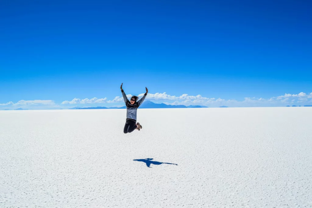 Voyageur sautant dans le désert de sel du Salar d’Uyuni en Bolivie, sous un ciel bleu éclatant, expérience insolite à inclure dans un travel planner Bolivie axé nature et aventure.