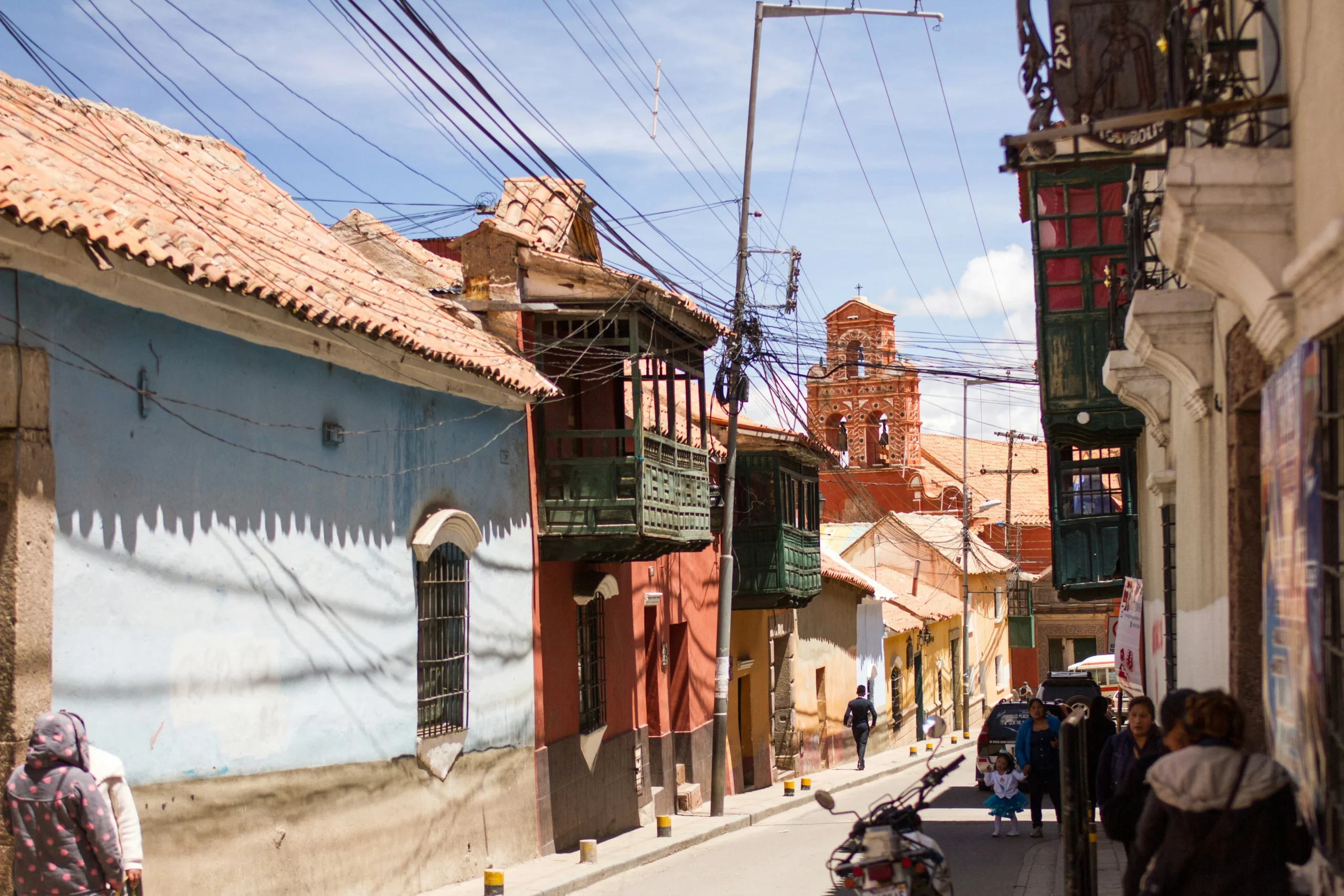 Rue étroite bordée de maisons coloniales colorées avec balcons en bois dans une ville historique de Bolivie, parfaite pour un travel planner Bolivie orienté patrimoine culturel et charme colonial.