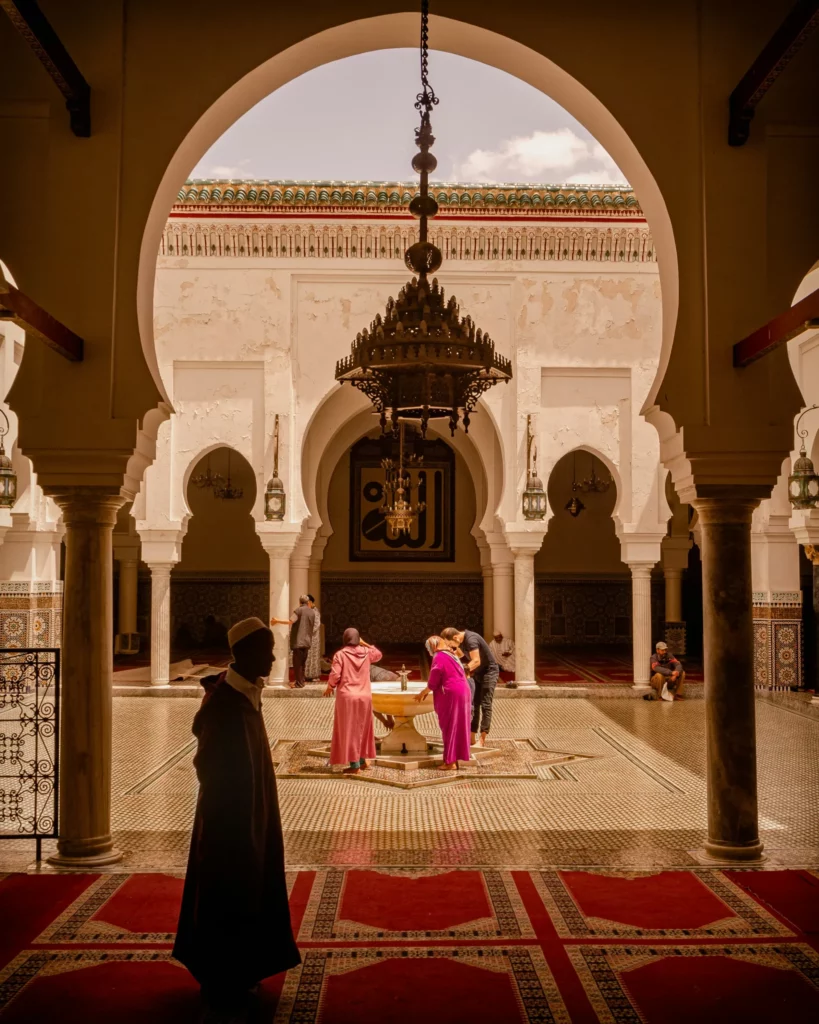 Visiteurs et fidèles dans une cour intérieure de mosquée traditionnelle au Maroc, avec ses arcades, mosaïques et fontaine, idéal pour un travel planner Maroc centré sur culture et patrimoine.