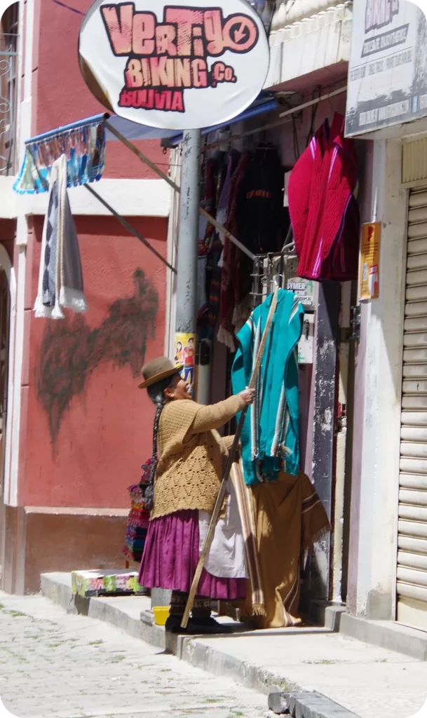 Femme bolivienne en tenue traditionnelle choisissant des vêtements dans une boutique de rue à La Paz, moment typique d’un itinéraire de voyage personnalisé centré sur l’artisanat et la culture locale.