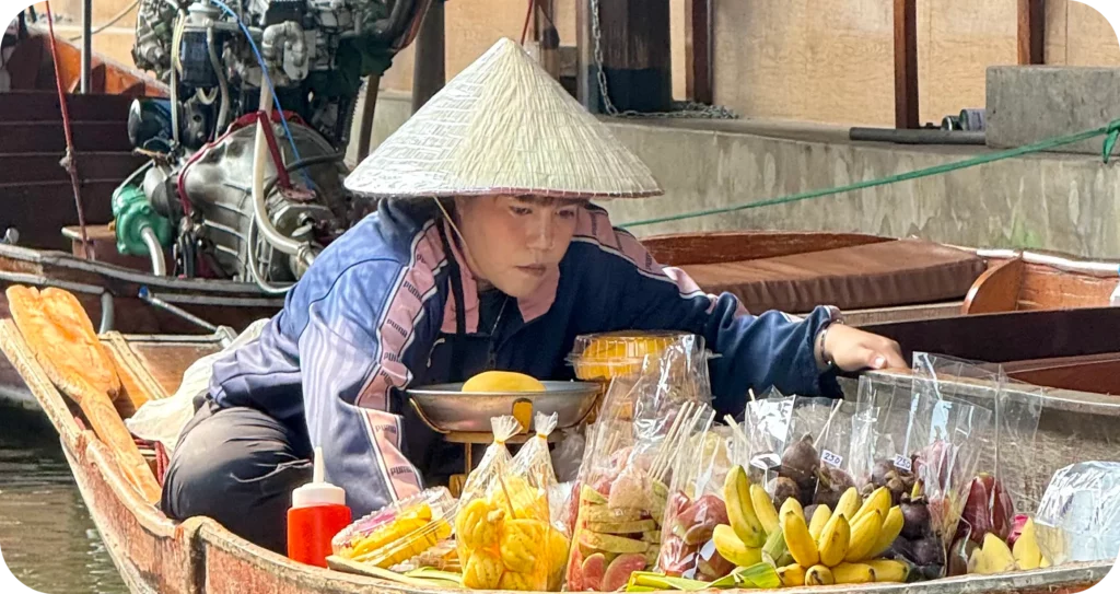 Scène authentique d’un marché flottant en Asie du Sud-Est, avec une vendeuse en chapeau conique sur sa barque remplie de fruits exotiques, lors d’un circuit organisé par un travel planner spécialisé en voyages culturels.
