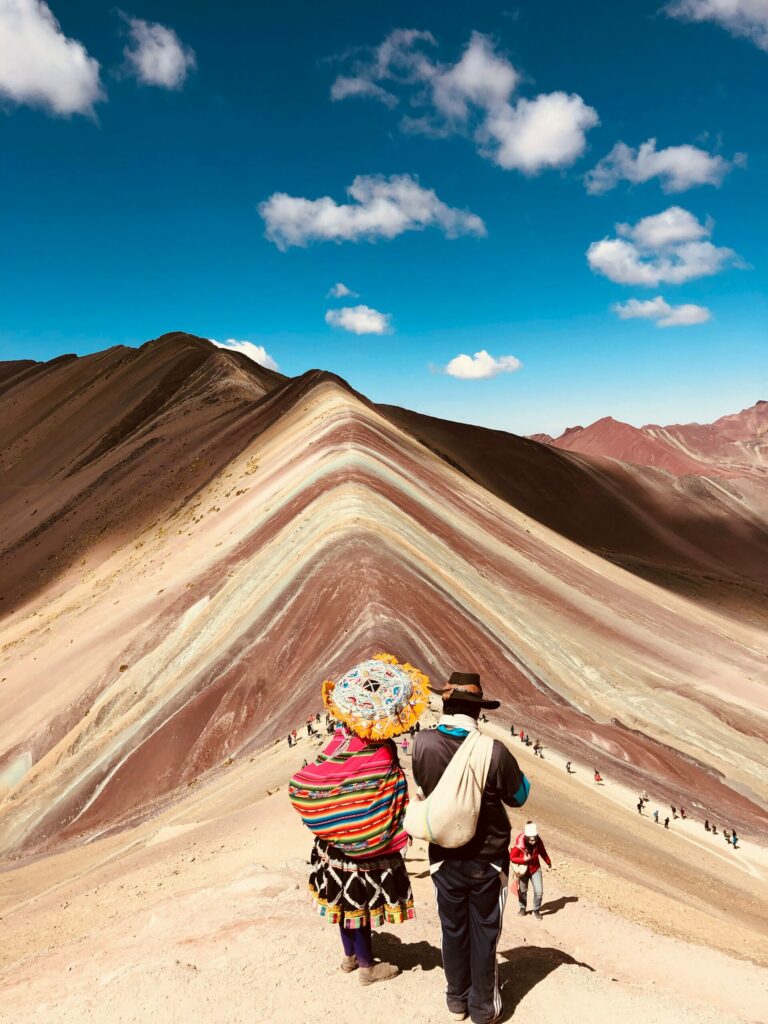 Couple de voyageurs face à la Rainbow Mountain au Pérou, entourés de paysages andins colorés, destination emblématique à intégrer dans un travel planner au Pérou pour une aventure inoubliable.