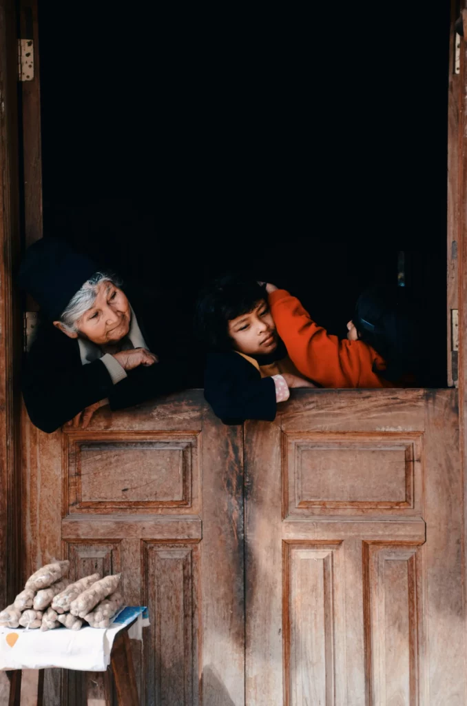 Scène de vie familiale à une fenêtre en bois en Bolivie, avec une grand-mère et deux enfants partageant un moment tendre, idéal pour un travel planner Bolivie centré sur les rencontres humaines et l’authenticité.