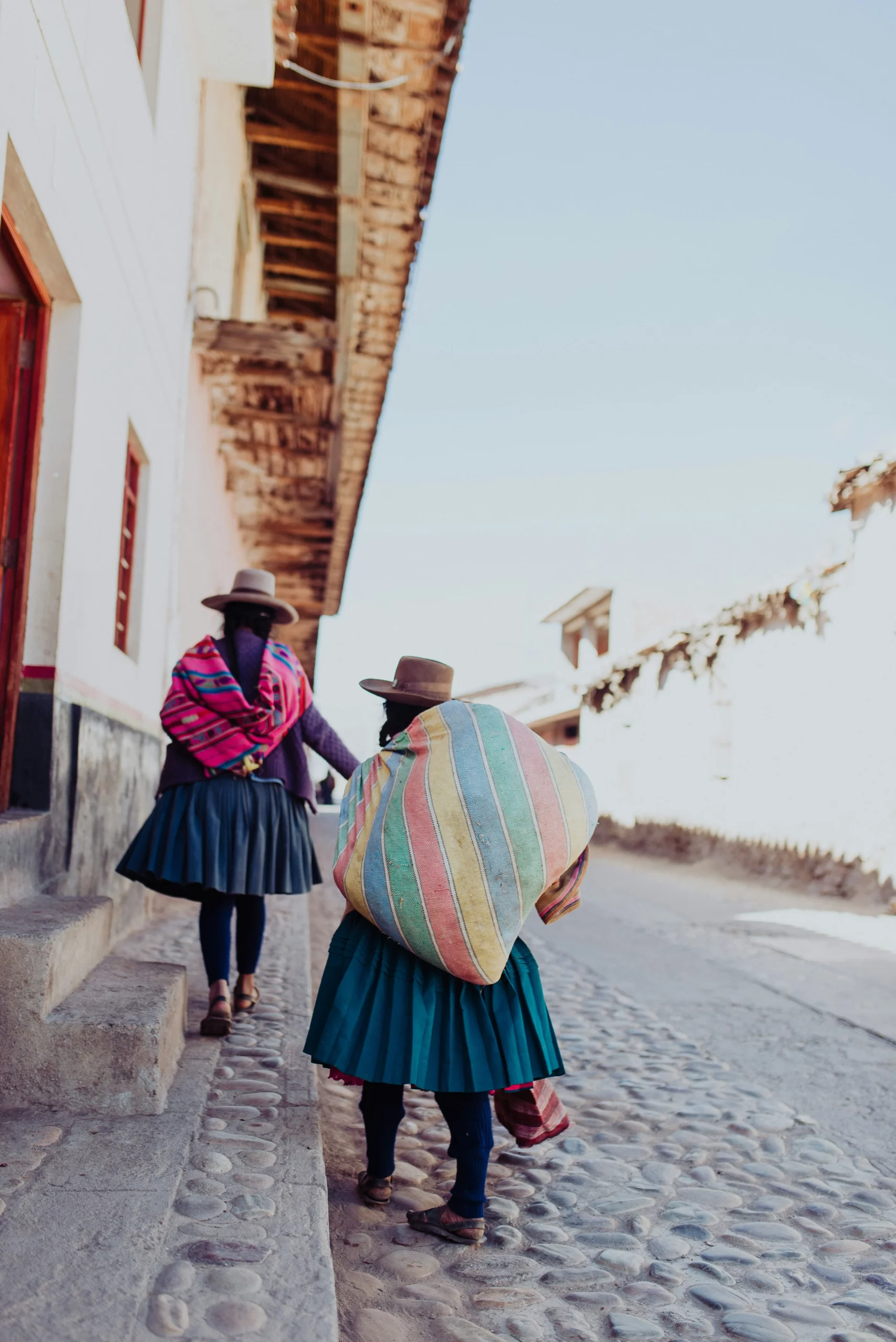 Femmes andines en habits traditionnels portant des mantas colorées dans une rue de village au Pérou, scène authentique à intégrer dans un travel planner péruvien orienté culture locale.