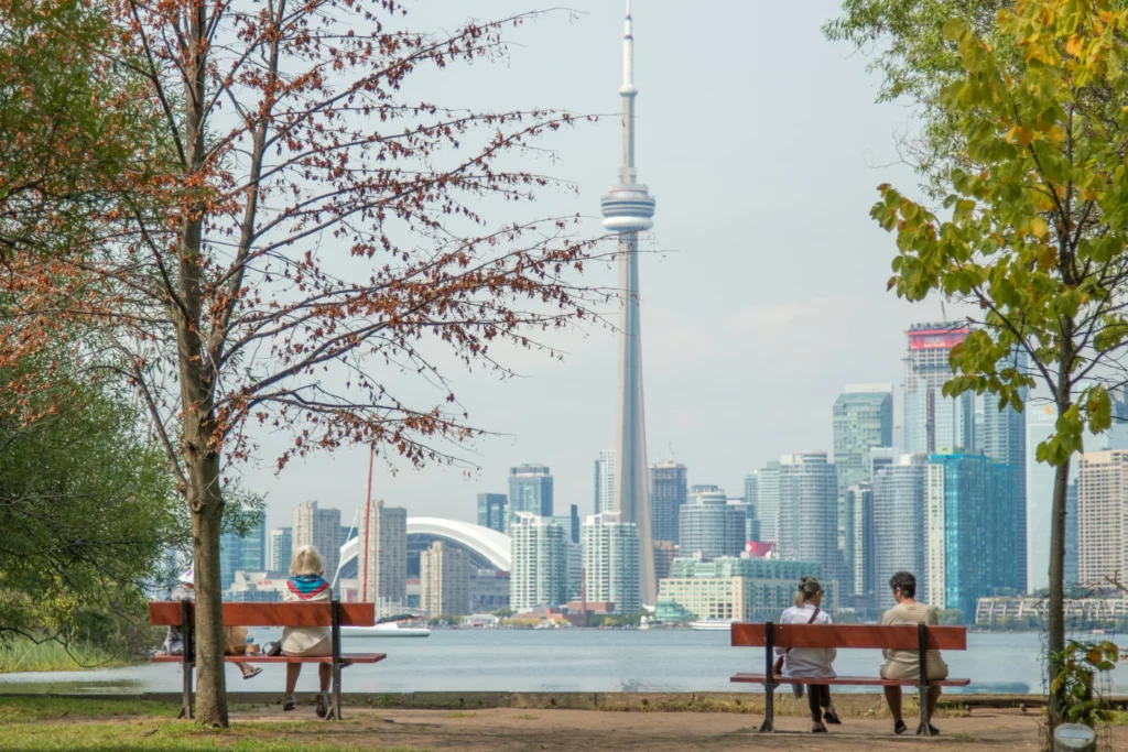 Vue panoramique sur la tour CN et les gratte-ciels de Toronto depuis une rive arborée, une étape urbaine à inclure dans un travel planner Canada.