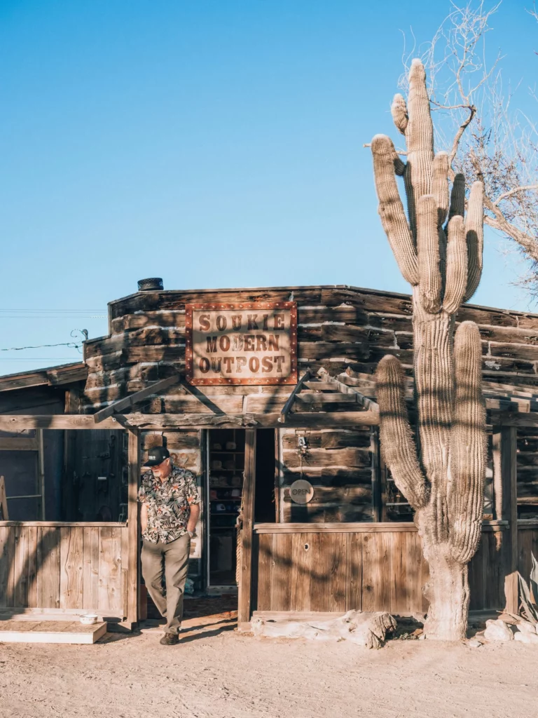 Boutique en bois rustique nommée "Soukie Modern Outpost", située dans un décor désertique typique du Sud-Ouest américain, idéale pour un travel planner Ouest américain axé authenticité et lieux insolites.